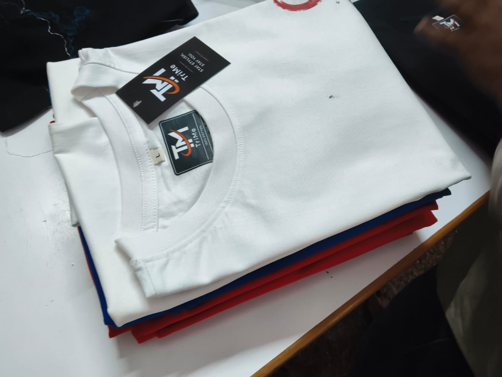 Folded white TRI/ME tee on a colour-sorted stack